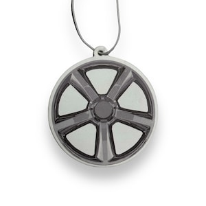 May include: A round car air freshener with a silver and black design of a car wheel with five spokes.