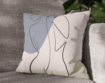 May include: Square throw pillow with a minimalist line art design. The pillow features a black outline of a figure against a light blue and beige backdrop. The pillow is on a gray sofa.