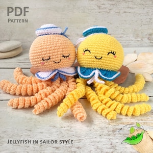 Puede incluir: Dos juguetes de medusa de crochet con sombreros de marinero. Las medusas son de color naranja y amarillo con detalles en blanco y azul. El texto "Jellyfish in Sailor Style" está en la parte inferior de la imagen.