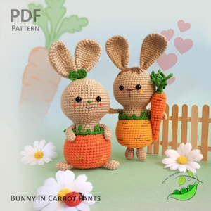 May include: Two crocheted bunny amigurumi toys wearing carrot costumes. The bunny on the left is wearing a carrot costume with green leaves around the waist. The bunny on the right is holding a carrot in its hand and wearing a carrot costume with green leaves around the waist. The bunnies are sitting on a green surface with a white picket fence in the background.
