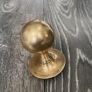 May include: A brass door knob featuring a spherical handle and a circular base. The knob has a polished finish. The door hardware is made of brass and is likely for interior or exterior use. The knob's dimensions are in centimetres.