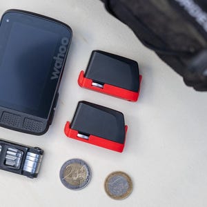 Könnte beinhalten: Eine Sammlung von Fahrradzubehör, darunter ein schwarzer Wahoo Fahrradcomputer, zwei schwarz-rote Sensoren, ein Multitool, Reifenheber und schwarzes Lenkerband. Zwei Euro-Münzen sind ebenfalls vorhanden.
