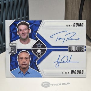 May include: A rectangular sports trading card featuring portraits of Tony Romo and Tiger Woods. The card includes the text Elite, Duo Duos, Tony Romo, and Tiger Woods, along with blue ink signatures from both individuals and a Dallas Cowboys star logo.