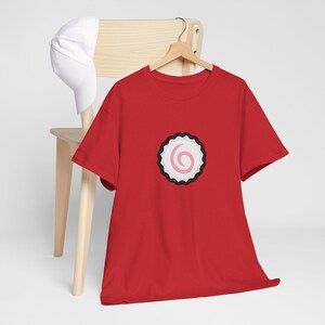 Peut inclure: T-shirt rouge à manches courtes avec un motif de gâteau de poisson kamaboko blanc et rose sur le devant.