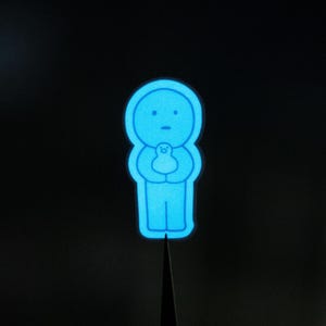 May include: A blue glow-in-the-dark sticker of a person holding a smaller person. The sticker is on a black background.