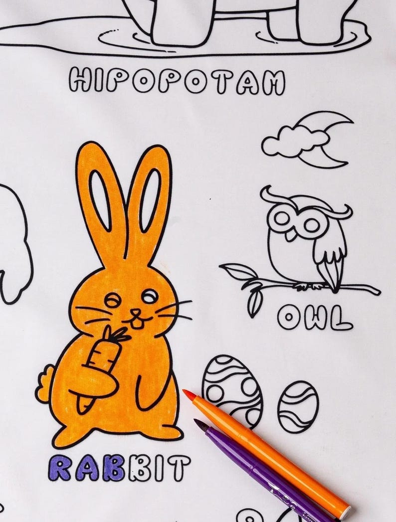 May include: A coloring page with an orange rabbit holding a carrot, an owl on a branch, and two eggs. The words "RABBIT", "OWL", and "HIPOPOTAM" are written on the page. Two colored markers are on the page.