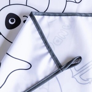 May include: A white fabric play mat with a gray border. The mat features black and white line drawings of animals, including a panda, a fish, and a banana.