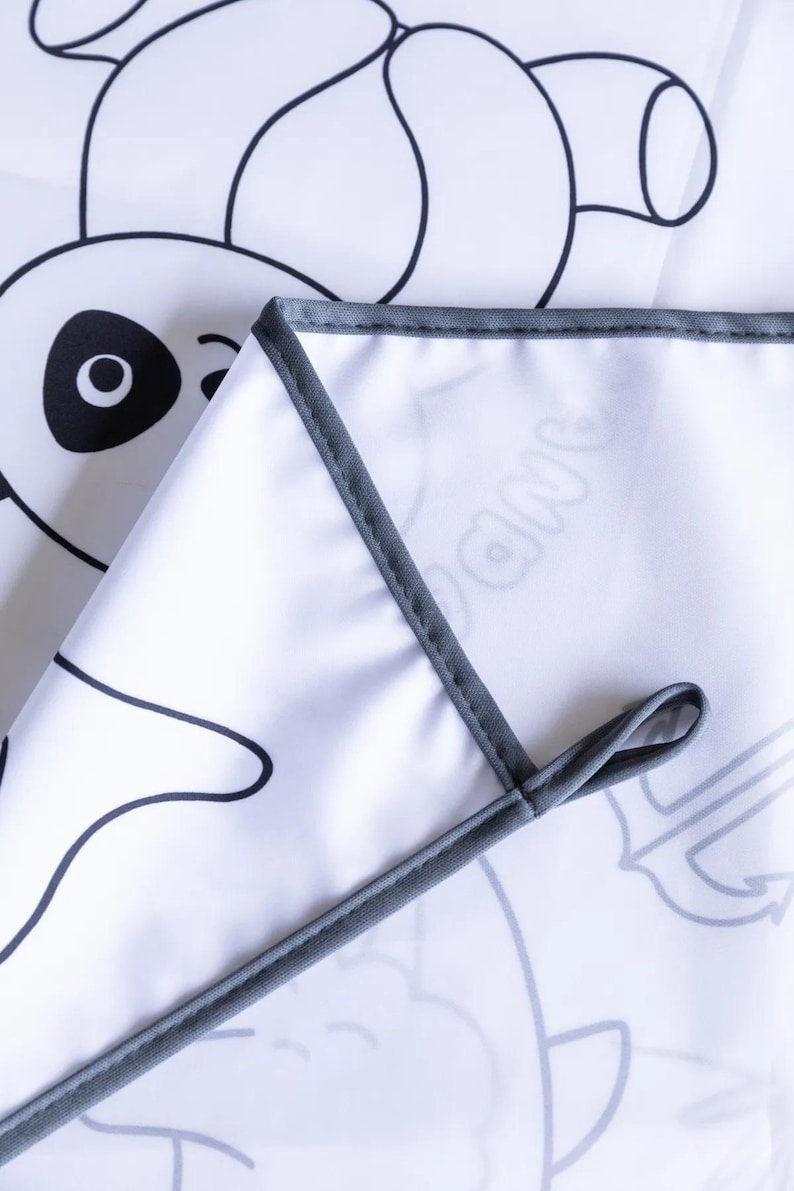 May include: A white fabric play mat with a gray border. The mat features black and white line drawings of animals, including a panda, a fish, and a banana.