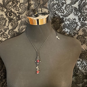 Könnte beinhalten: Eine schwarze Halskette mit einem Anhänger mit einer roten Rose und einem geometrischen Design mit roten und silbernen Akzenten. Die Halskette wird auf einer schwarzen Schaufensterpuppe präsentiert.