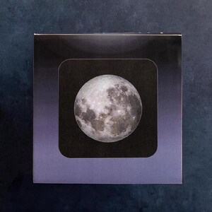 May include: A close-up of a black and white image of the moon in a square frame with a purple border.