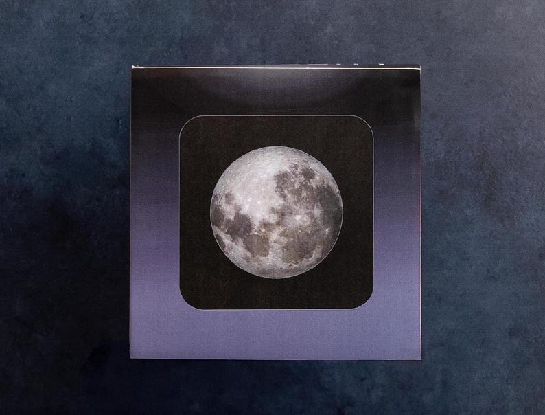 May include: A close-up of a black and white image of the moon in a square frame with a purple border.