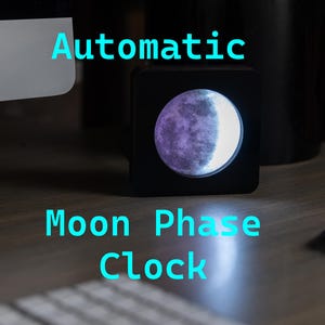 May include: A black moon phase clock with a white and purple moon graphic. The clock is on a wooden surface and says "Automatic Moon Phase Clock" in blue text.