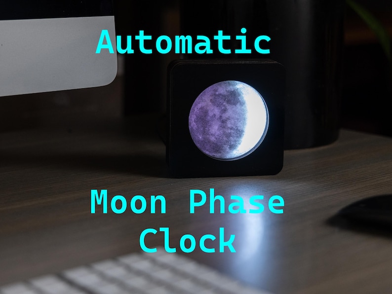 May include: A black moon phase clock with a white and purple moon graphic. The clock is on a wooden surface and says "Automatic Moon Phase Clock" in blue text.