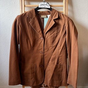 May include: A brown blazer with two front pockets and three buttons. The blazer is hanging on a wooden rack. The tag reads "Isabella's".