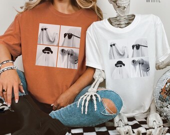 May include: Two t-shirts, one yam-colored and one white, each featuring a four-panel graphic of ghosts wearing sunglasses and hats. The word "YAM" is printed on the yam shirt, and "WHITE" on the white shirt. The shirts are casual wear.