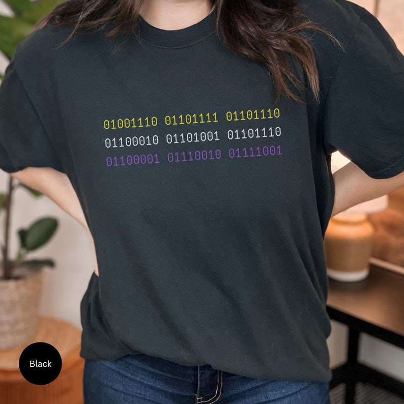 Puede incluir: Una camiseta negra con un dise&ntilde;o de c&oacute;digo binario morado y amarillo. El c&oacute;digo dice: 01001110 01110111 01101110 01100010 01101001 01101110 01100001 01110010 01111001