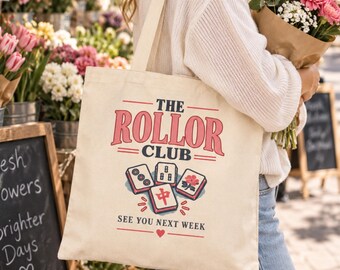 May include: A cream-colored canvas tote bag featuring the text THE ROLLOR CLUB and SEE YOU NEXT WEEK in dark blue and pink. The design includes an illustration of four mahjong tiles with red, blue, and pink details and a small red heart icon.