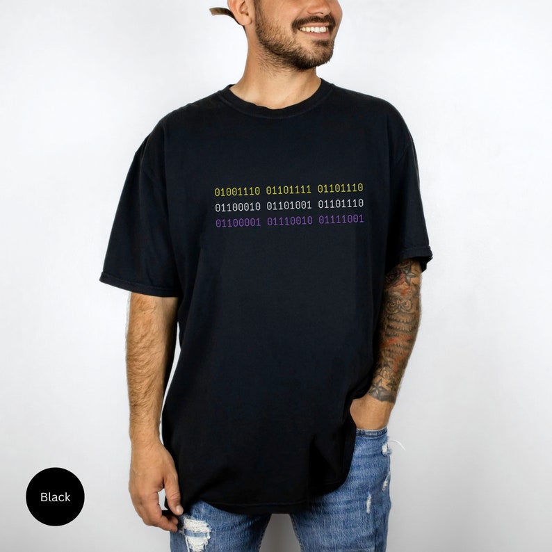 Puede incluir: Una camiseta negra con un gr&aacute;fico de c&oacute;digo binario en amarillo y morado. El c&oacute;digo dice: "01001110 01101111 01101110 01100010 01101001 01101110 01100001 01110010 01111001".