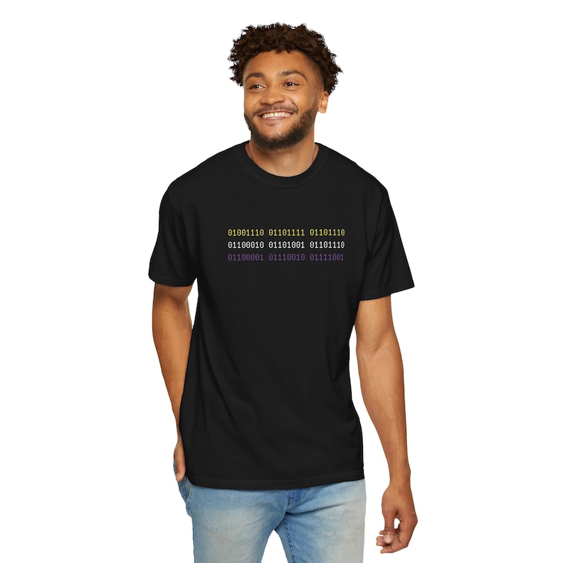 Nonbinary Agender person showing subtle pride by wearing techwear inspired nonbinary Comfort Colors t shirt in black with non-binary flag color text that reads in binary code, "nonbinary".