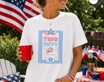 May include: White t-shirt with a graphic that says "TWO FIFTY" in blue and light blue, with stars and the years 1776-2026. The shirt is being worn outdoors with an American flag in the background.