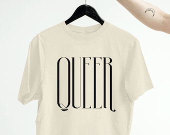 Puede incluir: Una camiseta corta de color crema con la palabra "QUEER" impresa en negro en la parte delantera.