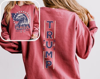 May include: Crimson red long-sleeved sweatshirt with a vertical graphic of the word "TRUMP" in blue with stars and numbers 45 and 47. The back of the sweatshirt has a graphic of an eagle with the words "MAGA 45-47" in white.