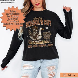 May include: Black long-sleeve tee with a graphic featuring a raccoon riding a goose, cacti, and the text "Giddy Up School's Out". The tee also has the text "Skedaddle" and "Go on now...Git".