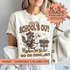 May include: Ivory-colored t-shirt with a graphic featuring a raccoon in a cowboy hat riding a goose, with text that reads "SCHOOL'S OUT." Additional text includes "K-5th GRADE AVAILABLE!" and "GO ON NOW...GIT."