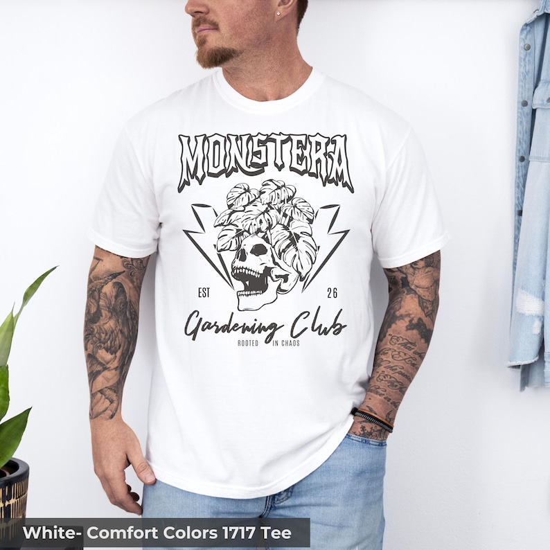 May include: White t-shirt with a black graphic featuring the word "MONSTERA" above a skull surrounded by leaves and lightning bolts. The text "Gardening Club" and "Rooted in Chaos" are below the skull. The shirt is a Comfort Colors 1717 Tee.
