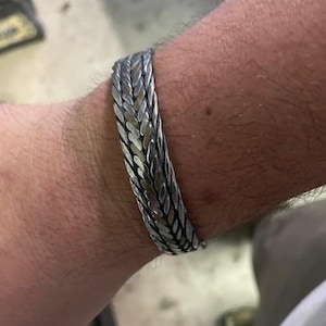May include: A silver and gold braided bracelet with a woven design.
