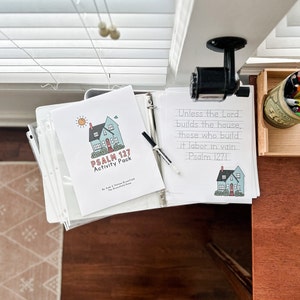 Puede incluir: Un paquete de actividades imprimible para niños con una casa azul con una puerta roja y un sol. El texto en la página dice "Psalm 127 Activity Pack". El texto en la otra página dice "Unless the Lord builds the house, those who build it labor in vain. Psalm 1271."