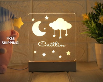 May include: A white acrylic night light with a moon, cloud, and stars design. The name "Caitlin" is written below the design. The light is on a wooden base.