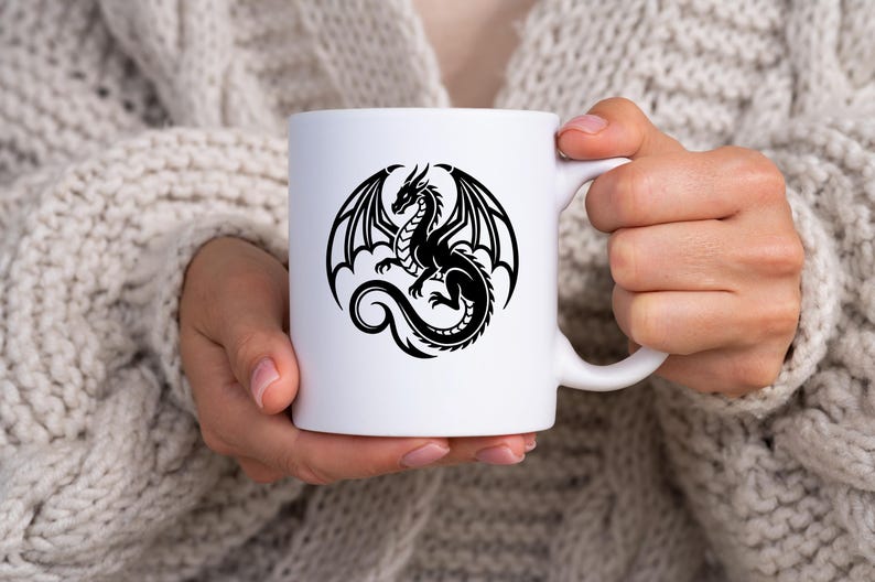 Puede incluir: Taza de cer&aacute;mica blanca con un dise&ntilde;o de drag&oacute;n negro. El drag&oacute;n tiene grandes alas y una larga cola. La taza la sostiene una persona que lleva un jersey color crema. La taza es de tama&ntilde;o est&aacute;ndar.