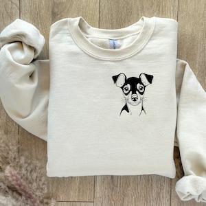 May include: A cream-colored sweatshirt with a black and white illustration of a small dog on the front.