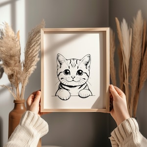 May include: A black and white line drawing of a cat peeking over the top of a frame. The cat has large eyes and a cute expression.