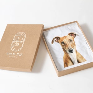 Puede incluir: Una caja de cart&oacute;n marr&oacute;n con un logotipo blanco que dice "WILD INK DIGITAL". La caja est&aacute; abierta y dentro hay una camiseta blanca con una ilustraci&oacute;n de un perro marr&oacute;n y blanco.
