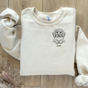 May include: A cream-coloured sweatshirt with a black line drawing of a dog on the front. The dog is looking at the viewer and has the name "Luna" written underneath it.