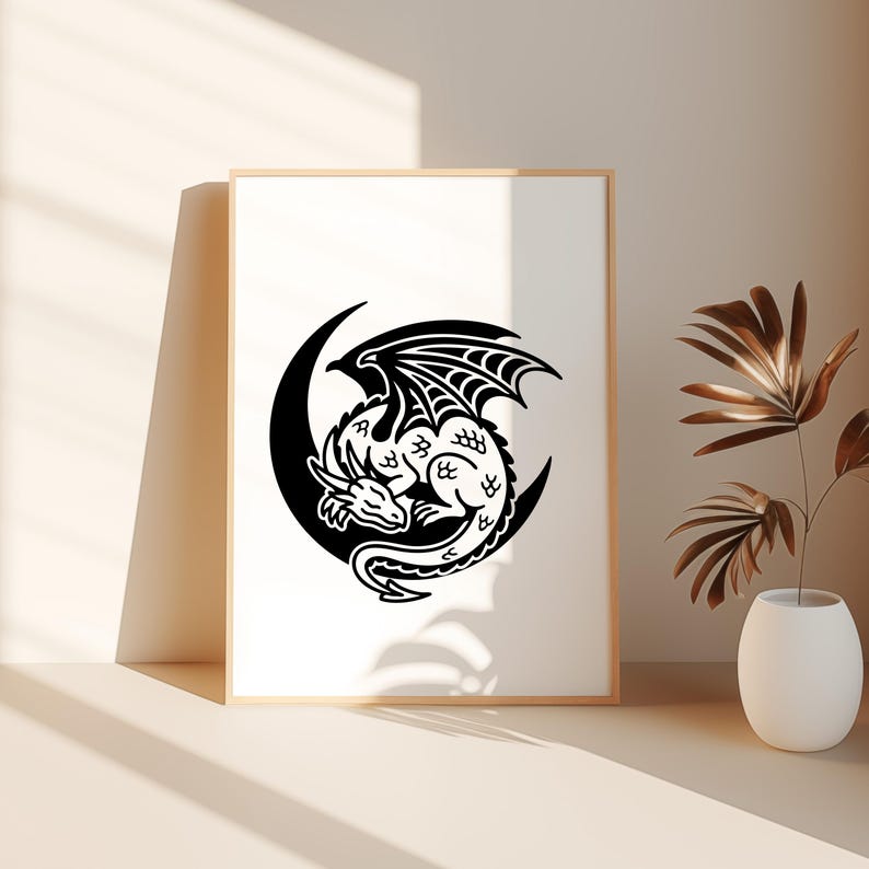 Puede incluir: Un estampado enmarcado con un dise&ntilde;o de drag&oacute;n en blanco y negro. El drag&oacute;n est&aacute; acurrucado dentro de una luna creciente. El drag&oacute;n tiene alas y escamas detalladas. La obra de arte se muestra en un marco de madera de color claro.