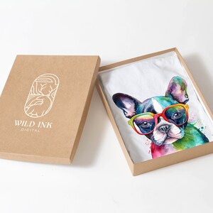 May include: A white t-shirt with a colorful watercolor illustration of a French bulldog wearing sunglasses. The t-shirt is packaged in a brown cardboard box with the logo "WILD INK DIGITAL" printed on the box.