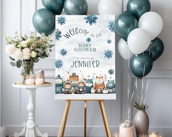 May include: Welcome to the Baby Shower of Mom-to-be Jennifer sign with a winter woodland theme. The sign features a blue and white background with snowflakes and cute animals wearing winter hats and scarves. The sign is displayed on a wooden easel with blue and white balloons in the background.