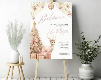 Pode incluir: Um cartaz de boas-vindas para um chá de bebê com um esquema de cores rosa e dourado. O cartaz apresenta uma ilustração em aquarela de uma árvore de Natal, uma rena e presentes. O texto no cartaz diz "Bem-vinda ao chá de bebê da futura mamãe Lela Phipps Sábado, 13 de janeiro de dois mil e vinte e quatro #mamalila".