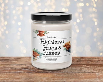 May include: A white candle jar with a black lid. The label says "Smells like Highland Hugs & Kisses" and features a cartoon illustration of a Highland cow. The text below the illustration says "thank you for coming to Sarah's Baby Shower 6 oz | 12 hours".