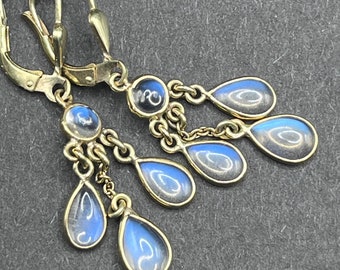 May include: Gold dangle earrings with a teardrop design. The earrings have multiple teardrop-shaped crystals that are clear with a blue iridescent sheen.