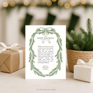 K&ouml;nnte beinhalten: Eine wei&szlig;e Weihnachtskarte mit einem gr&uuml;nen Kranzdesign und dem Text "HAPPY HOLIDAYS". Die Karte enth&auml;lt eine personalisierte Nachricht. Die Szene wird durch verpackte Geschenke und Gr&uuml;npflanzen erg&auml;nzt, was eine festliche Atmosph&auml;re schafft.