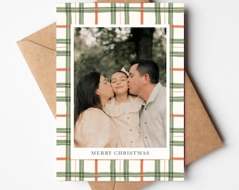 May include: Christmas card with a family photo inside a plaid border in green and orange. The words "MERRY CHRISTMAS" are printed at the bottom of the photo. The card is inside a brown envelope.