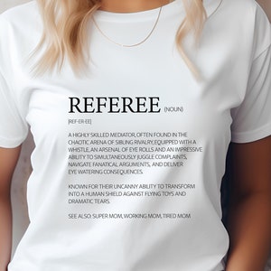 Könnte beinhalten: Weißes T-Shirt mit einem schwarzen Grafikdesign, das das Wort "Schiedsrichter" als einen hochqualifizierten Vermittler definiert, der oft in der chaotischen Arena der Geschwisterrivalität zu finden ist. Die Grafik enthält auch den Text "Siehe auch: Super Mama, Berufstätige Mama, Müde Mama."