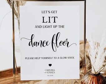 May include: A white sign in a gold frame with the text "Let's get lit and light up the dance floor. Please help yourself to a glow stick."  The sign also includes the names "Christina and Joshua" and the date "06.24XX".