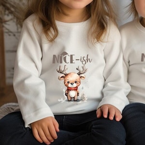May include: Two children wearing white long-sleeved shirts with a brown reindeer graphic and the text "nice-ish". They are both wearing white knit hats and sitting on a white and grey blanket.