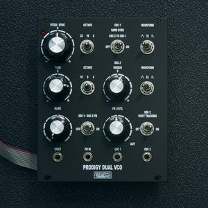 May include: A black synthesizer module with knobs, switches, and jacks. The module is labeled "Prodigy Dual VCO" and has labels for "Pitch/Sync", "Octave", "OSC 1", "Waveform", "Tune", "Unison", "Glide", "OSC 1-OSC 2 FM", "FM Level", "VIOCT", "FM In", "OSC 1", "OSC 2", "Out", and "VIOCT Tracking".