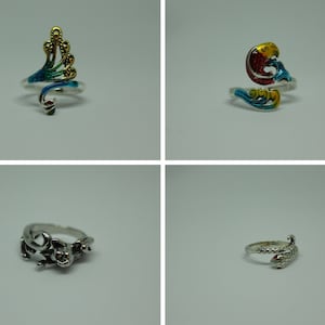 Könnte beinhalten: Vier silberne Ringe mit bunten Emaille-Designs. Die Ringe zeigen einen Pfau, einen Vogel, ein Eidechse und eine Schlange.